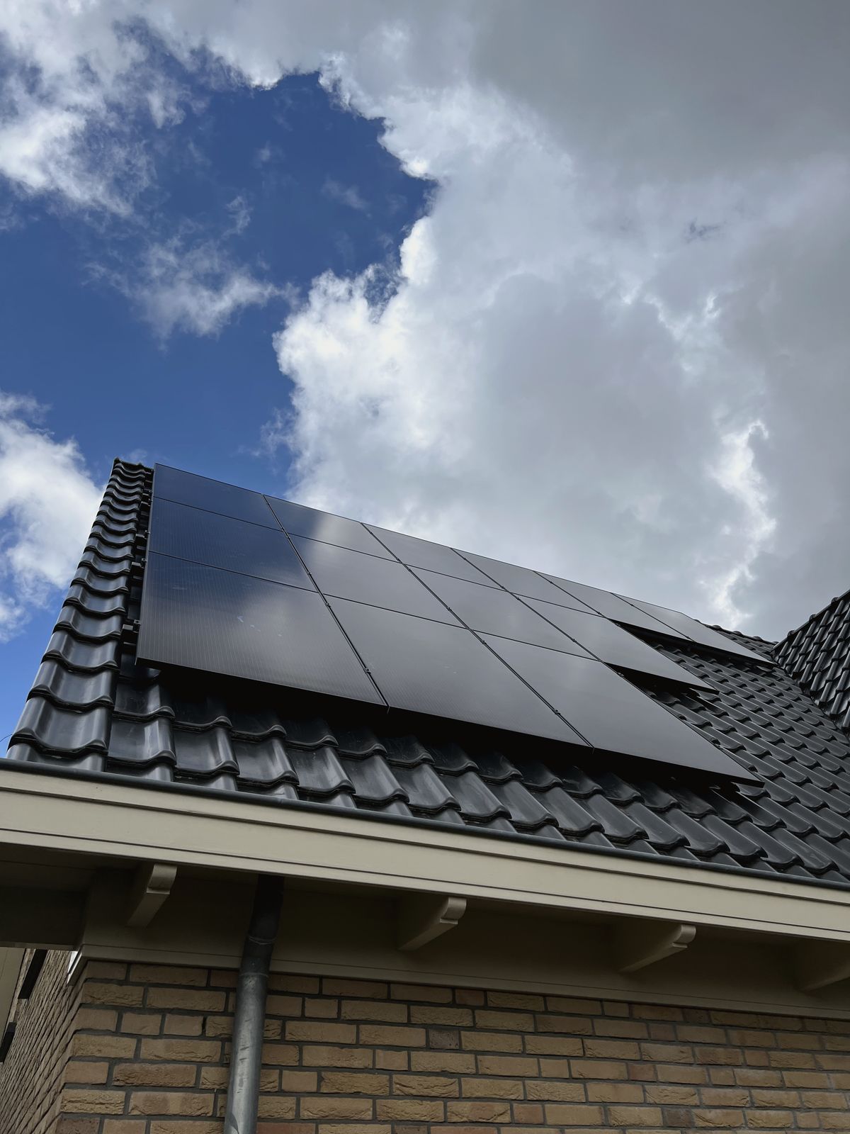 Zwarte zonnepanelen op het pannendak van een woning in Haarlem, tegen een blauwe lucht met wolken.